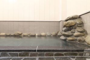 A stone-lined hot spring bath with a tiled wall and a stone ledge. - Kusatsu Onsen 326 Yamanoyu Hotel (Kusatsu)