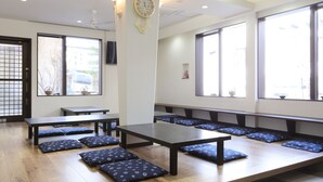 A room with wooden flooring, multiple tables and benches, large windows, and a wall-mounted clock. - Kusatsu Onsen 326 Yamanoyu Hotel (Kusatsu)