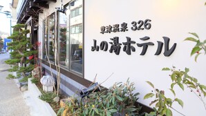 A building with a sign in Japanese, a window, and some plants. - Kusatsu Onsen 326 Yamanoyu Hotel (Kusatsu)