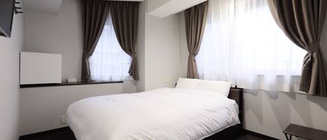 Una habitación de hotel con cama, mesita de noche, televisor y cortinas.