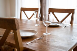 A wooden dining table with two chairs, a wine glass, a fork, and a plate.