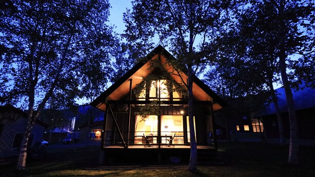 A small, cozy cabin with a sloped roof, surrounded by trees, and a lit interior visible through the windows. - Bliss Cottage SAKURA (Kutchan)