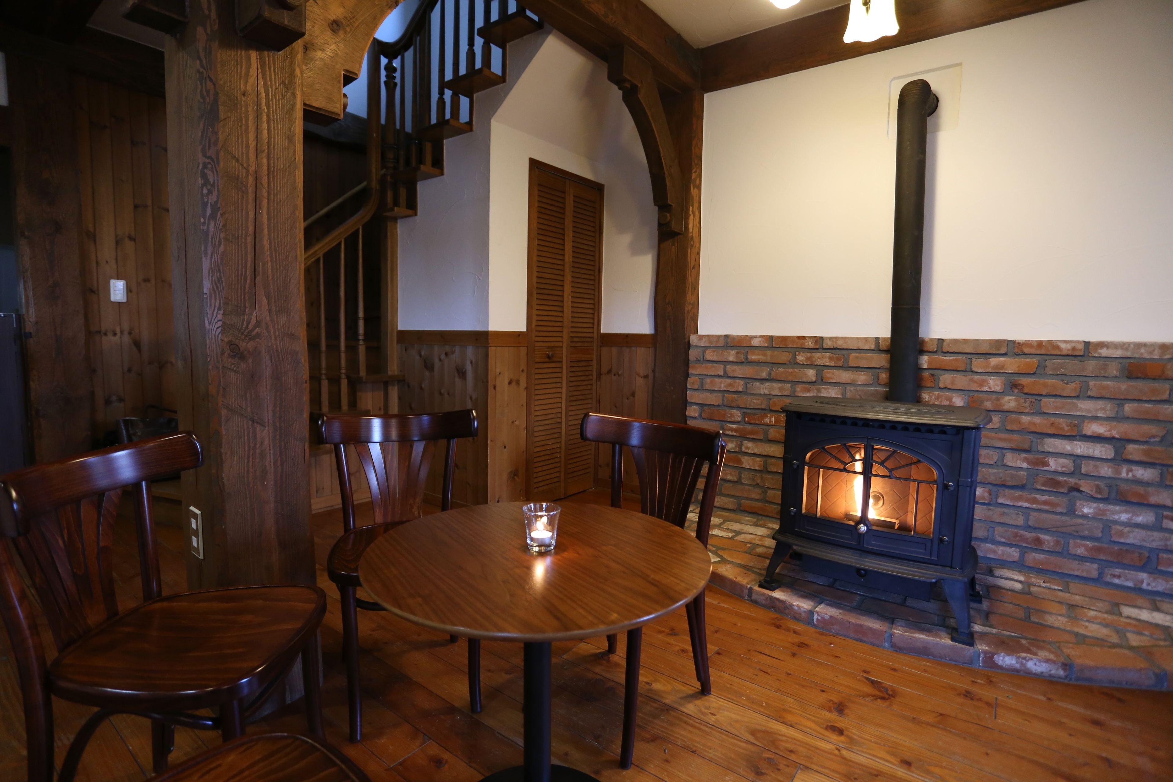 Un comedor de madera con chimenea de ladrillo, sillas de madera y una escalera.