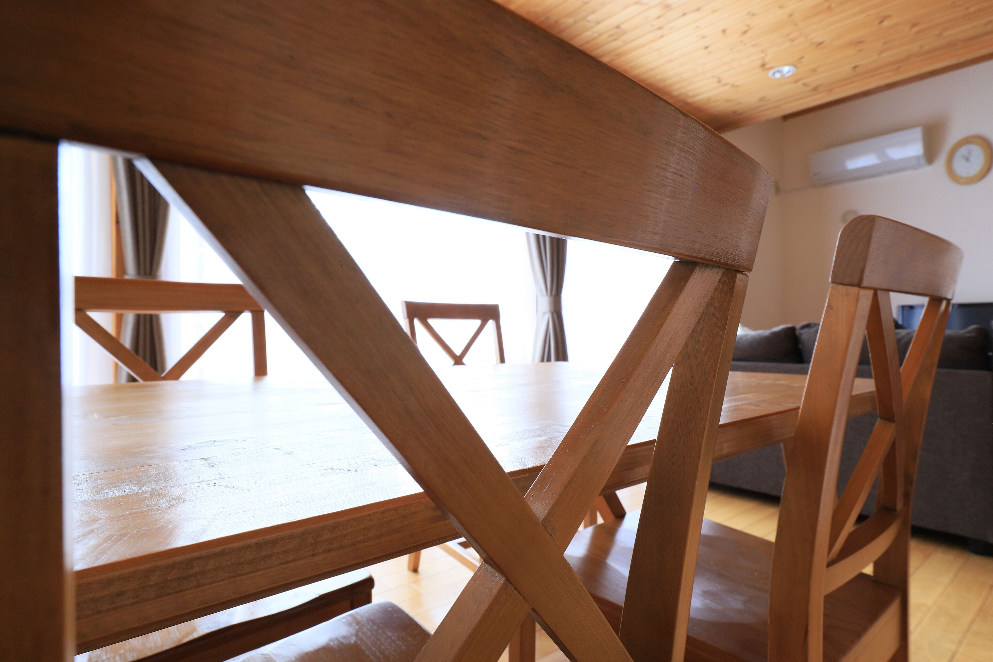 A wooden dining table with a cross-back design, a wooden chair, and a sofa in a room with wooden flooring and a sloped ceiling.