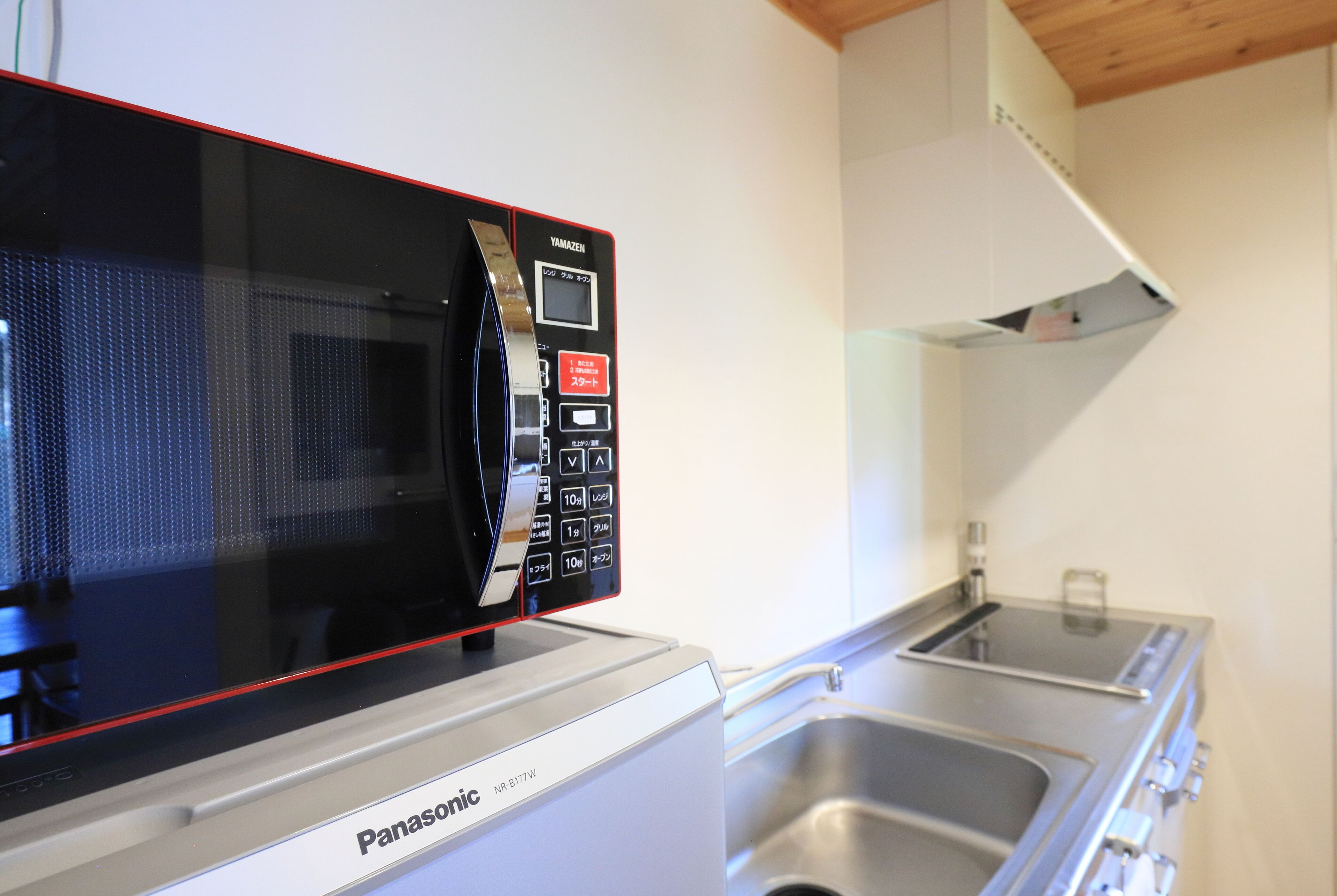 A Panasonic microwave oven with a digital display and control panel, placed on a white kitchen counter with a stainless steel sink.
