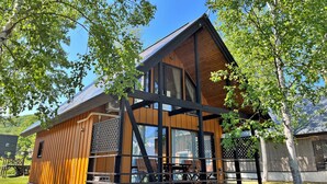 A wooden cabin with a large window, a balcony, and a dining area. - Bliss Cottage SAKURA (Kutchan)