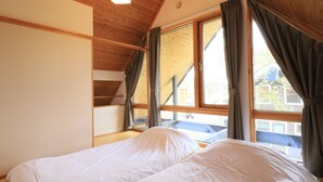 A bedroom with a wooden ceiling, a large window with curtains, and a bed with white bedding. - Bliss Cottage SAKURA (Kutchan)