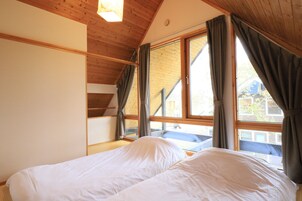 A bedroom with a wooden ceiling, a large window with curtains, and a bed with white bedding.