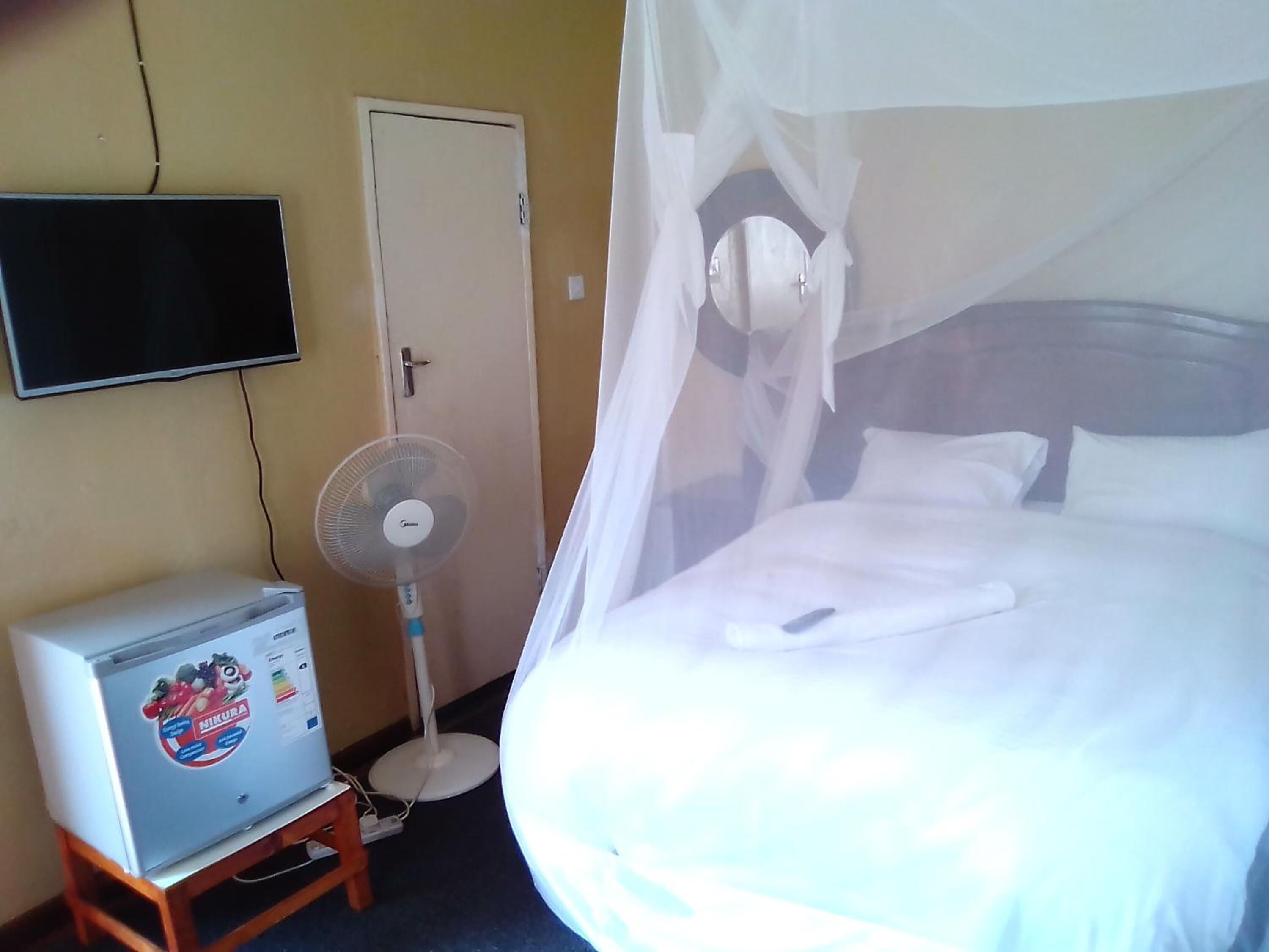 A hotel room with a bed, a television mounted on the wall, a small air conditioner, and a standing fan.