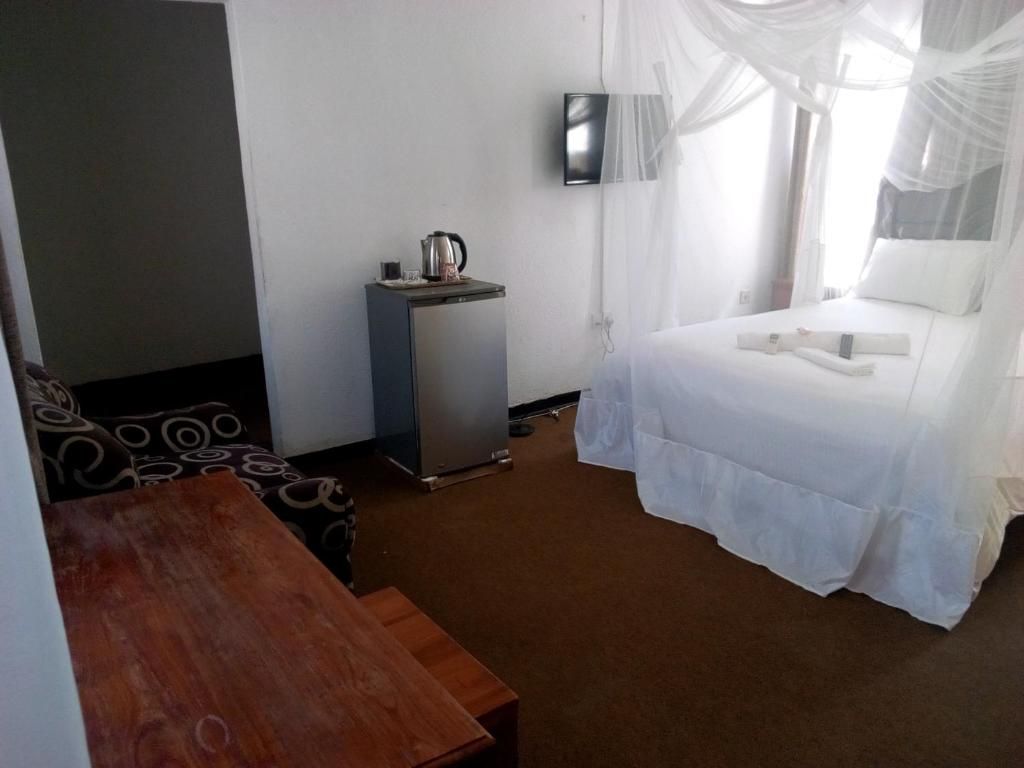Una habitación de hotel con cama, un escritorio pequeño, un televisor y una ventana con cortinas translúcidas.