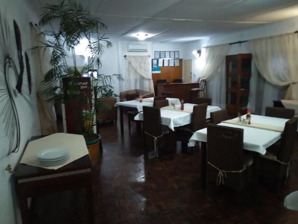 Comedor con mesas dispuestas para cuatro personas, una planta grande en maceta y una recepción al fondo.