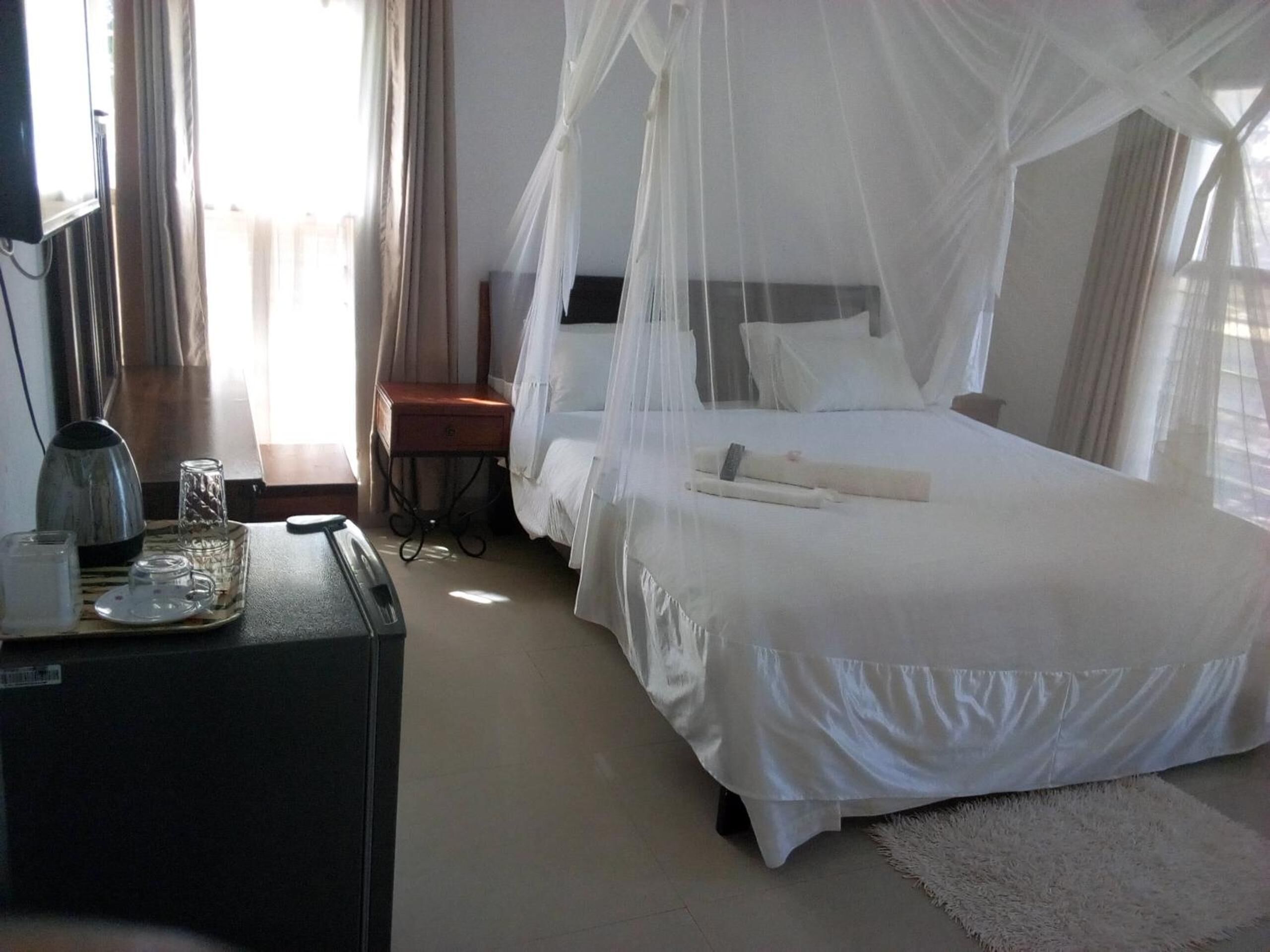 Une chambre d’hôtel avec un lit sous un baldaquin blanc, une table de chevet avec une lampe, un petit bureau et une chaise.