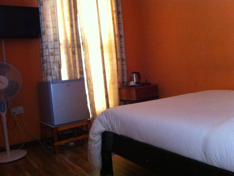 Quarto com cama, um ventilador, uma mesinha com chaleira e televisão em móvel.
