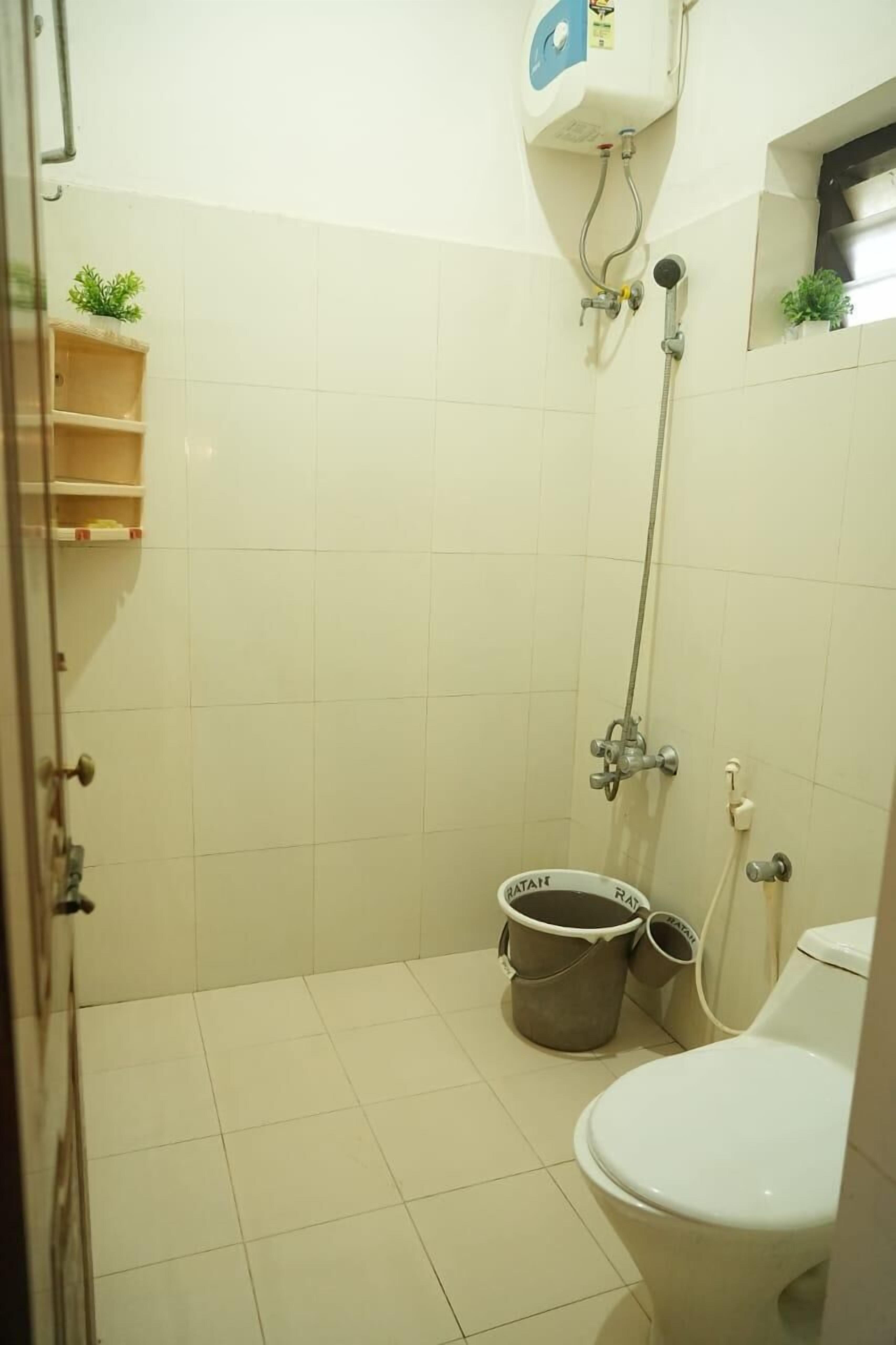 A small, tiled bathroom with a shower, toilet, and a bucket.