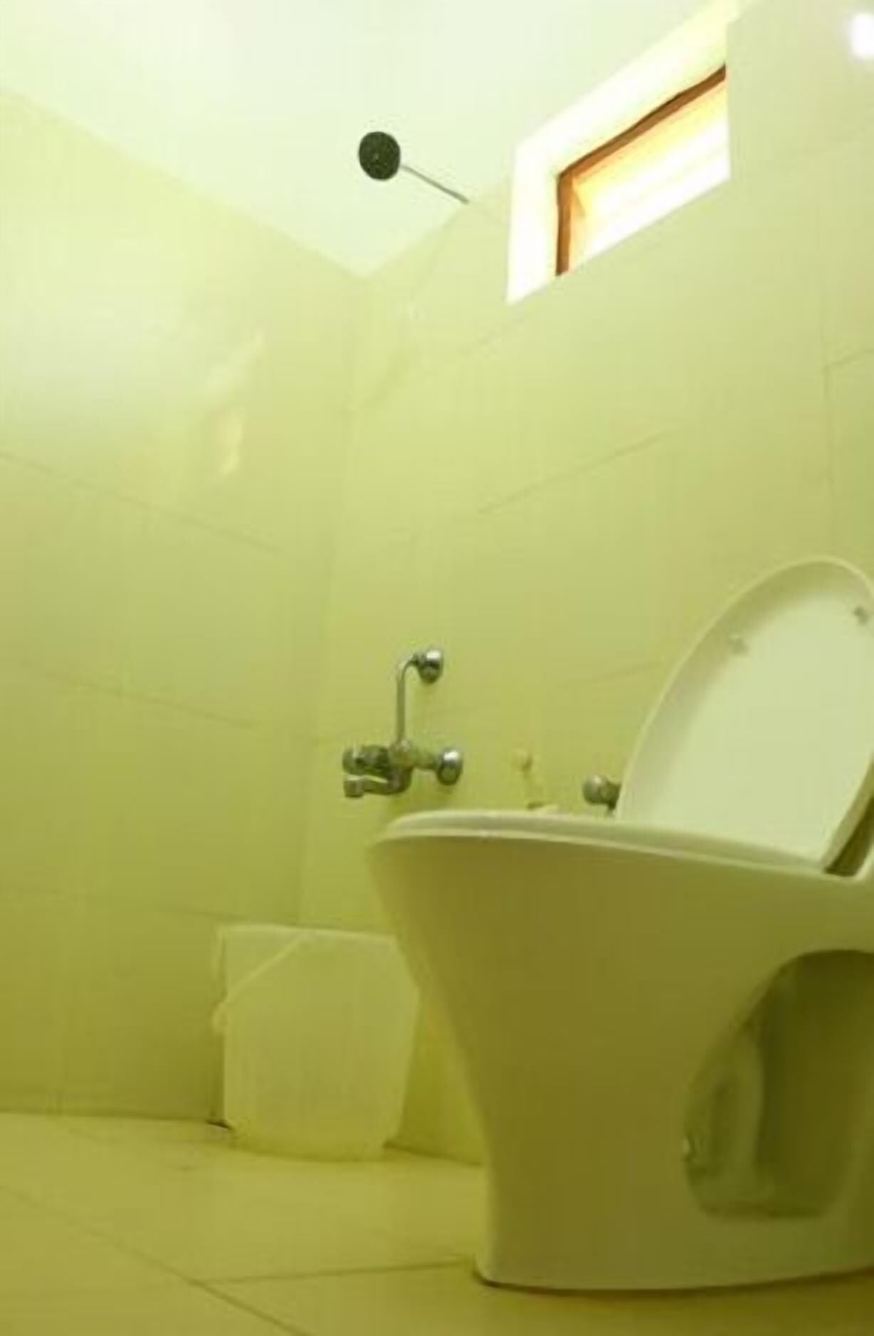 A bathroom with a toilet, a small window, and a wall-mounted light fixture.