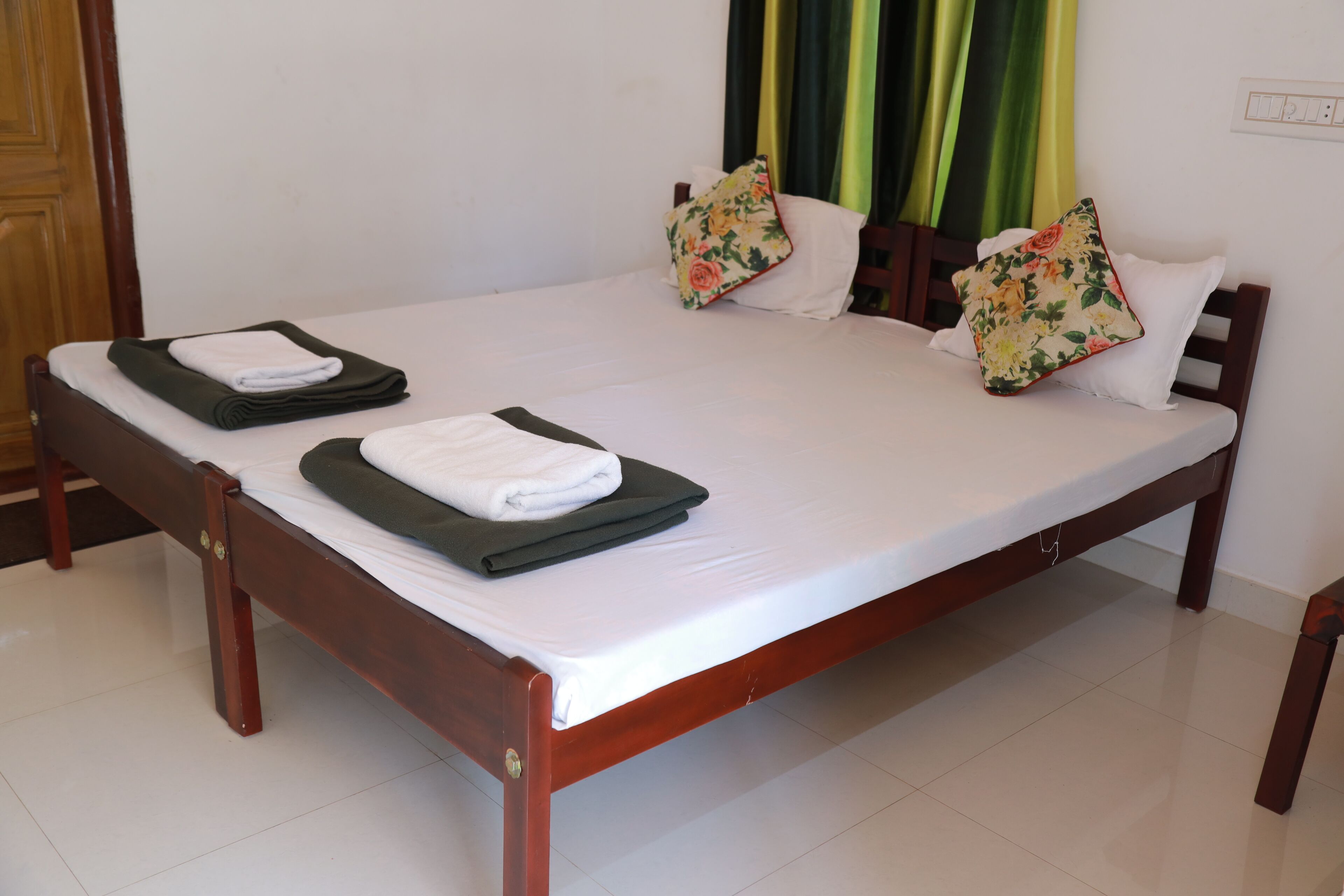 Una cama doble con sábanas blancas, dos almohadas estampadas con motivos florales y dos toallas dobladas.