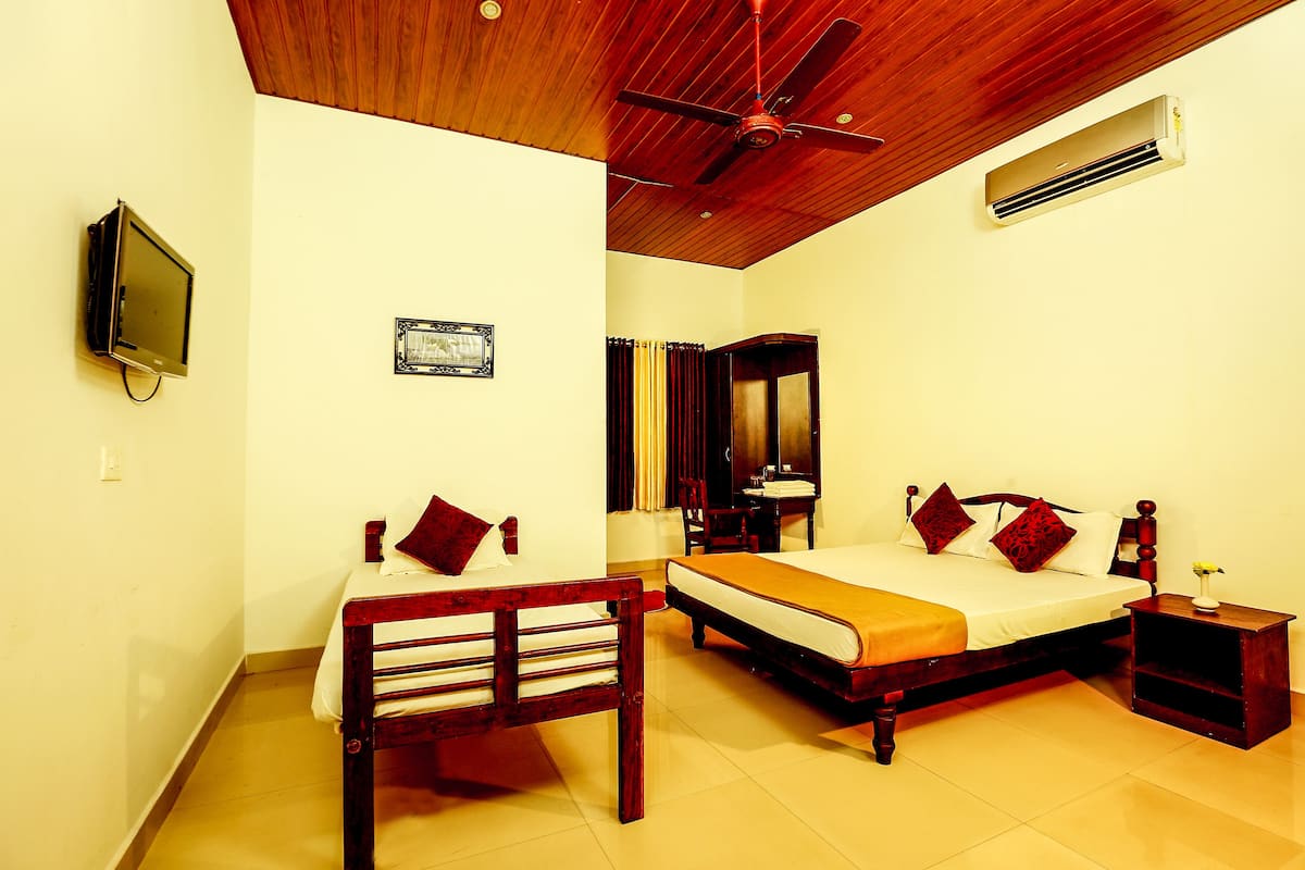 A bedroom with two beds, a ceiling fan, an air conditioner, a television, and a small table with a vase.