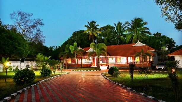 A traditional building with a red roof and white walls, surrounded by lush greenery and palm trees. - Baywatch Beach Resort (Ambalapuzha)