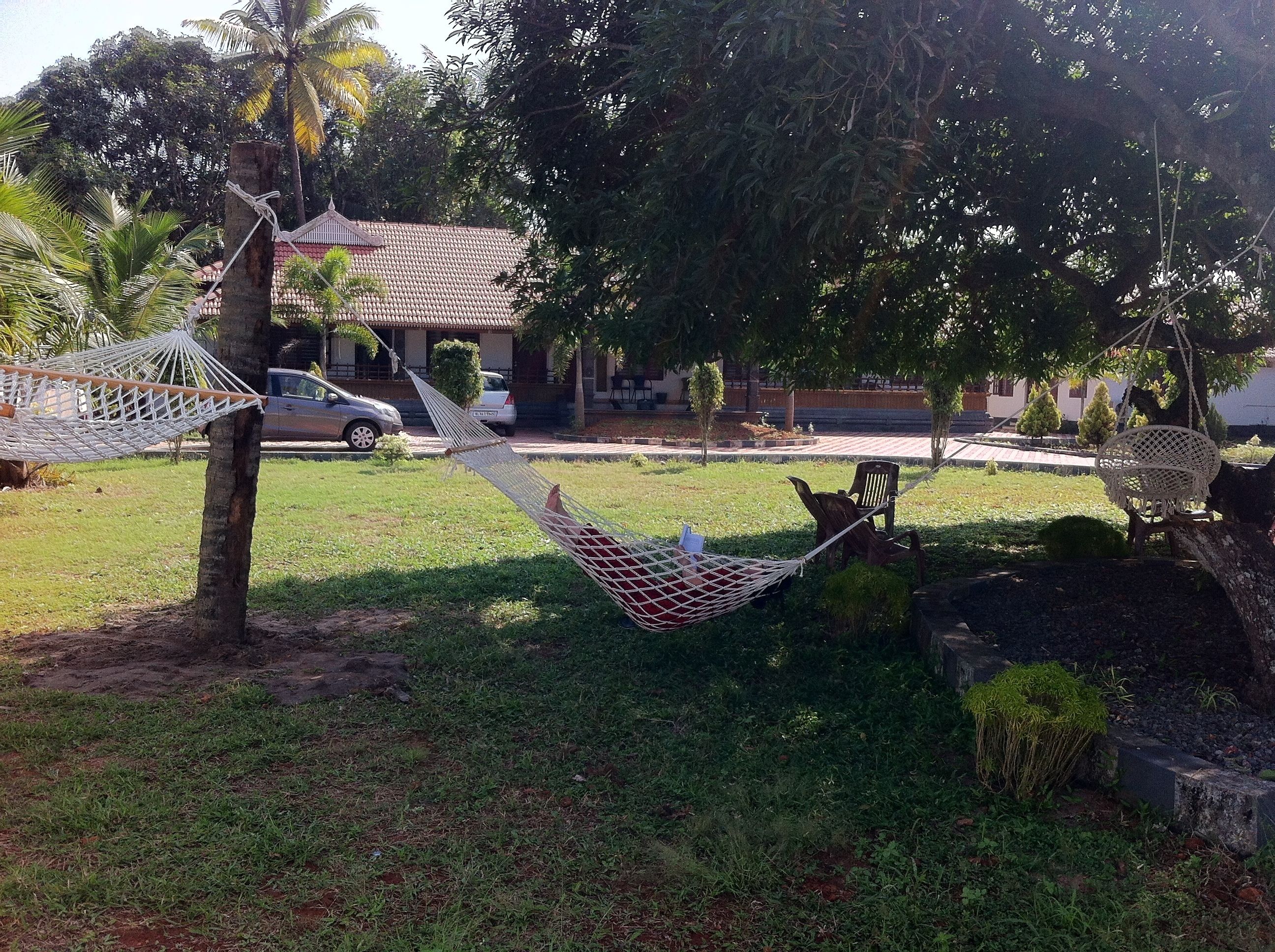 A hammock and a chair in a grassy area with a building in the background.