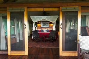 A room with a bed, two chairs, a red rug, and a wooden floor. - Selinda Camp (Selinda Reserve)