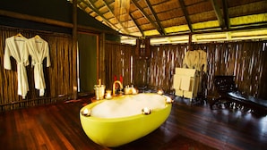 A spacious bathroom with a large bathtub, wooden floors, and a bamboo wall. - Selinda Camp (Selinda Reserve)