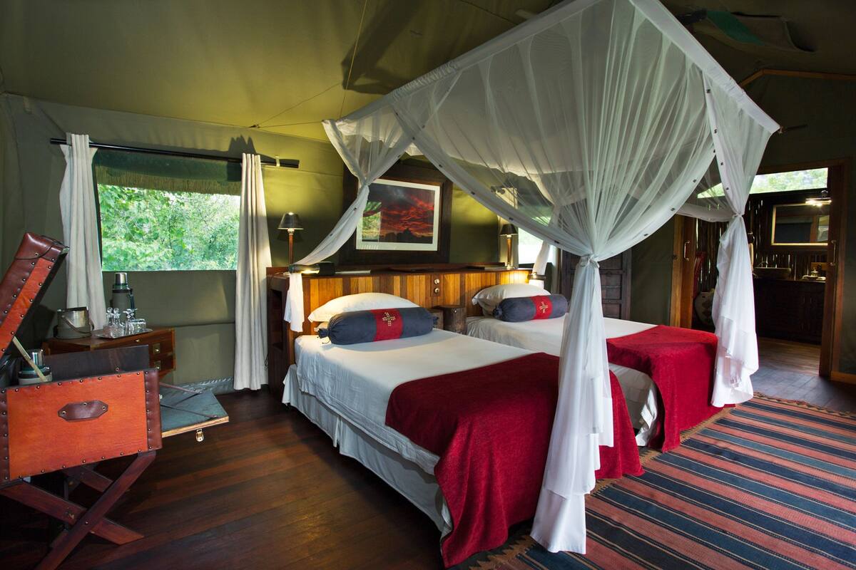 A room with two beds, each with a canopy, a wooden desk, and a window with curtains.