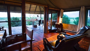 A room with a wooden floor, a large window, and a view of the outdoors. - Selinda Camp (Selinda Reserve)