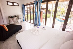 Une chambre d’hôtel dotée d’un grand lit, d’un petit canapé, d’un mini-bar et offrant une vue sur l’espace extérieur grâce à de grandes portes-fenêtres coulissantes.