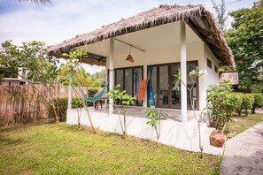 Une maison avec un toit de chaume, une véranda et un petit jardin agrémenté d’un hamac.