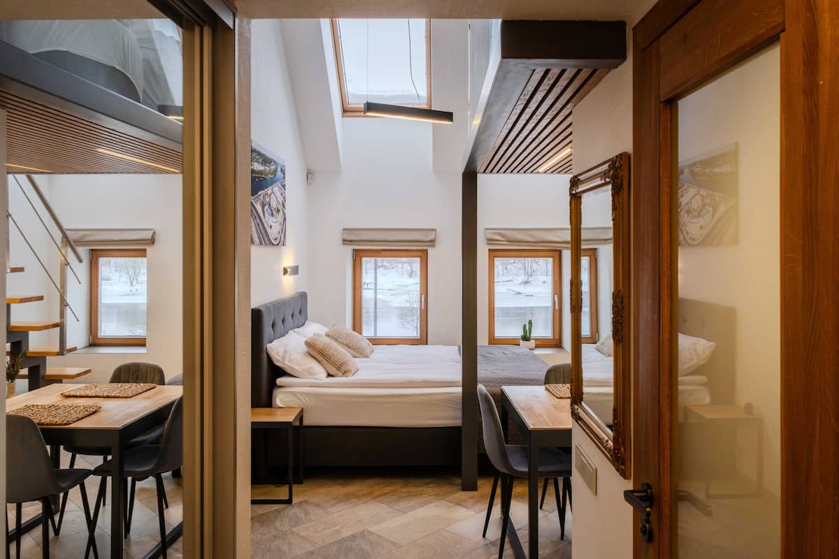 A bedroom with a bed, two bedside tables, a desk with chairs, a large mirror, and a skylight.