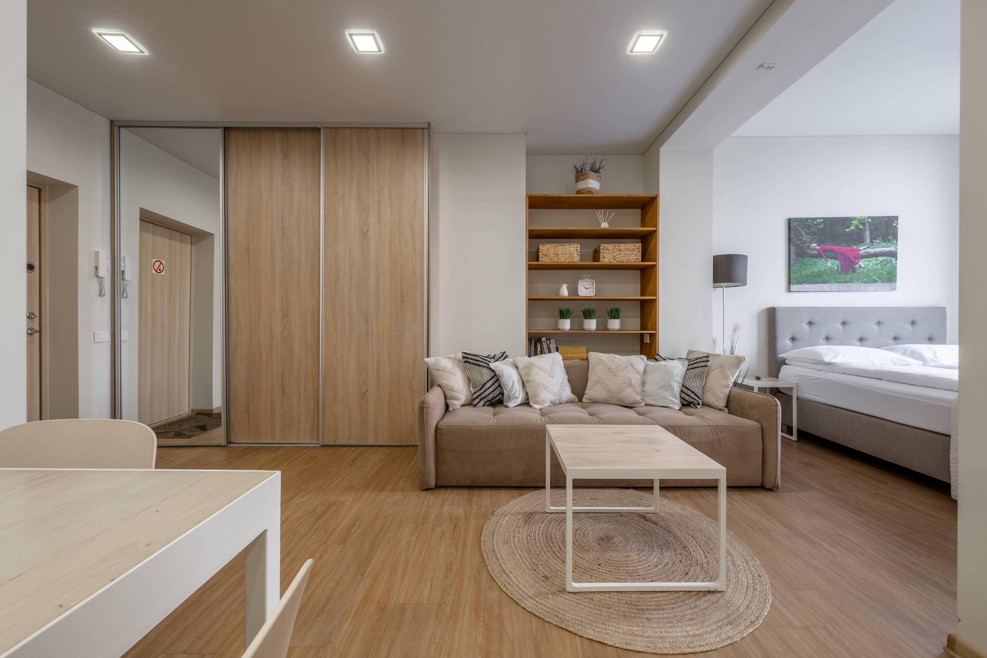 Una habitación moderna y bien iluminada con sofá, una mesita, una estantería y una cama.