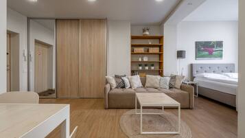 Una habitación moderna y bien iluminada con sofá, una mesita, una estantería y una cama.