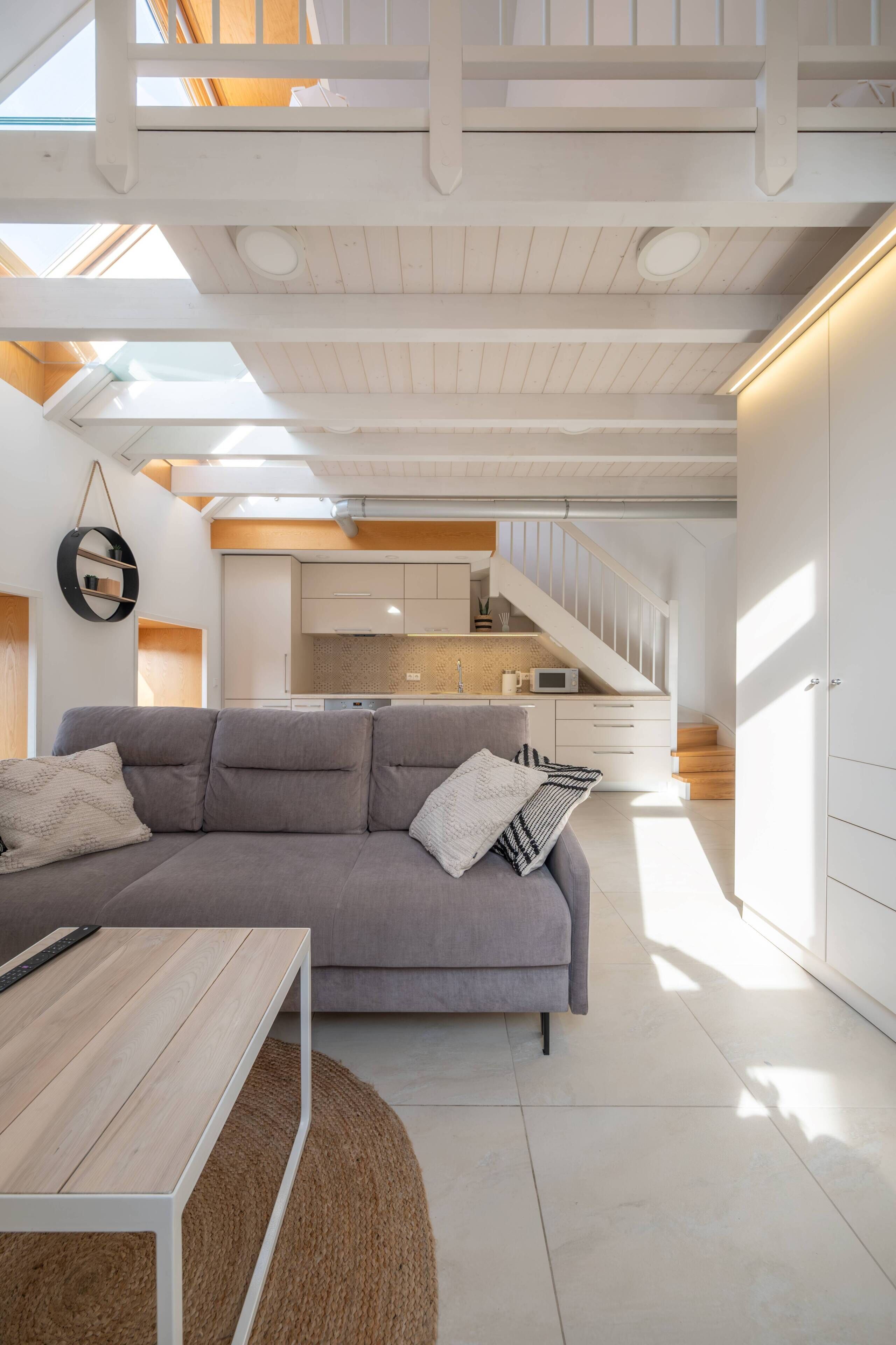 Un intérieur moderne avec un canapé gris, une table basse en bois et un coin cuisine à l’arrière-plan.