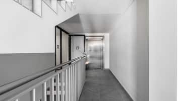 A modern, clean hallway with a metal railing, a staircase, and an elevator.