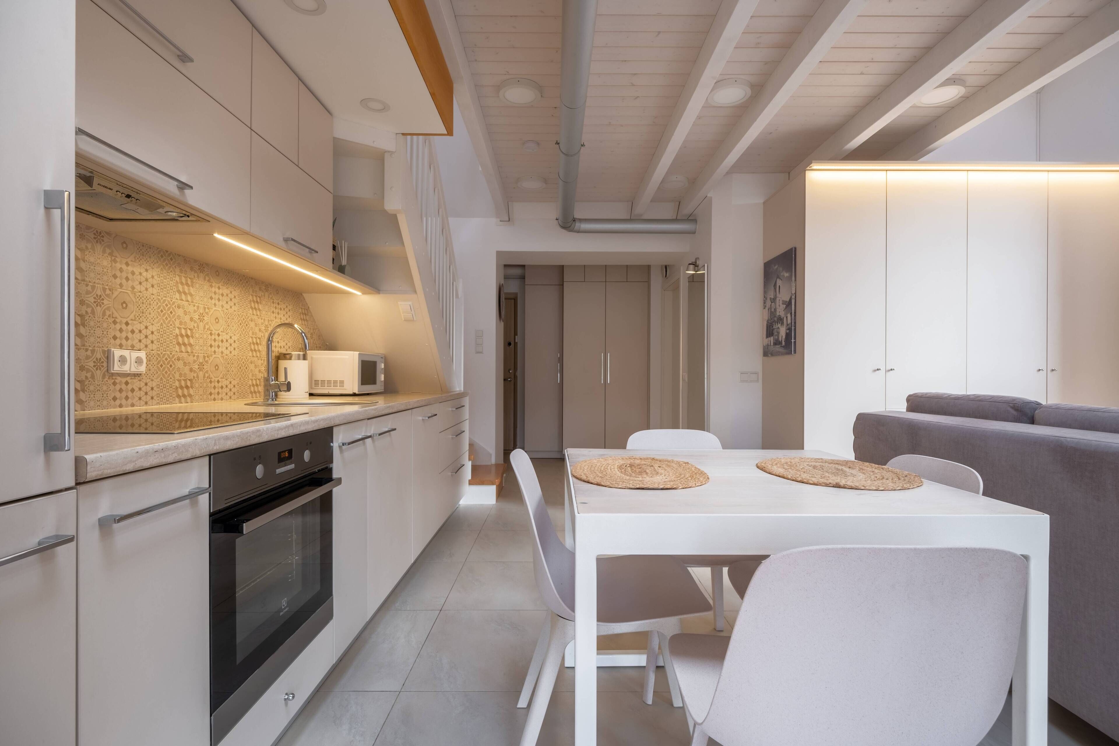 Een moderne keuken met witte kastjes, een ingebouwde oven en een eethoek met een witte tafel en stoelen.