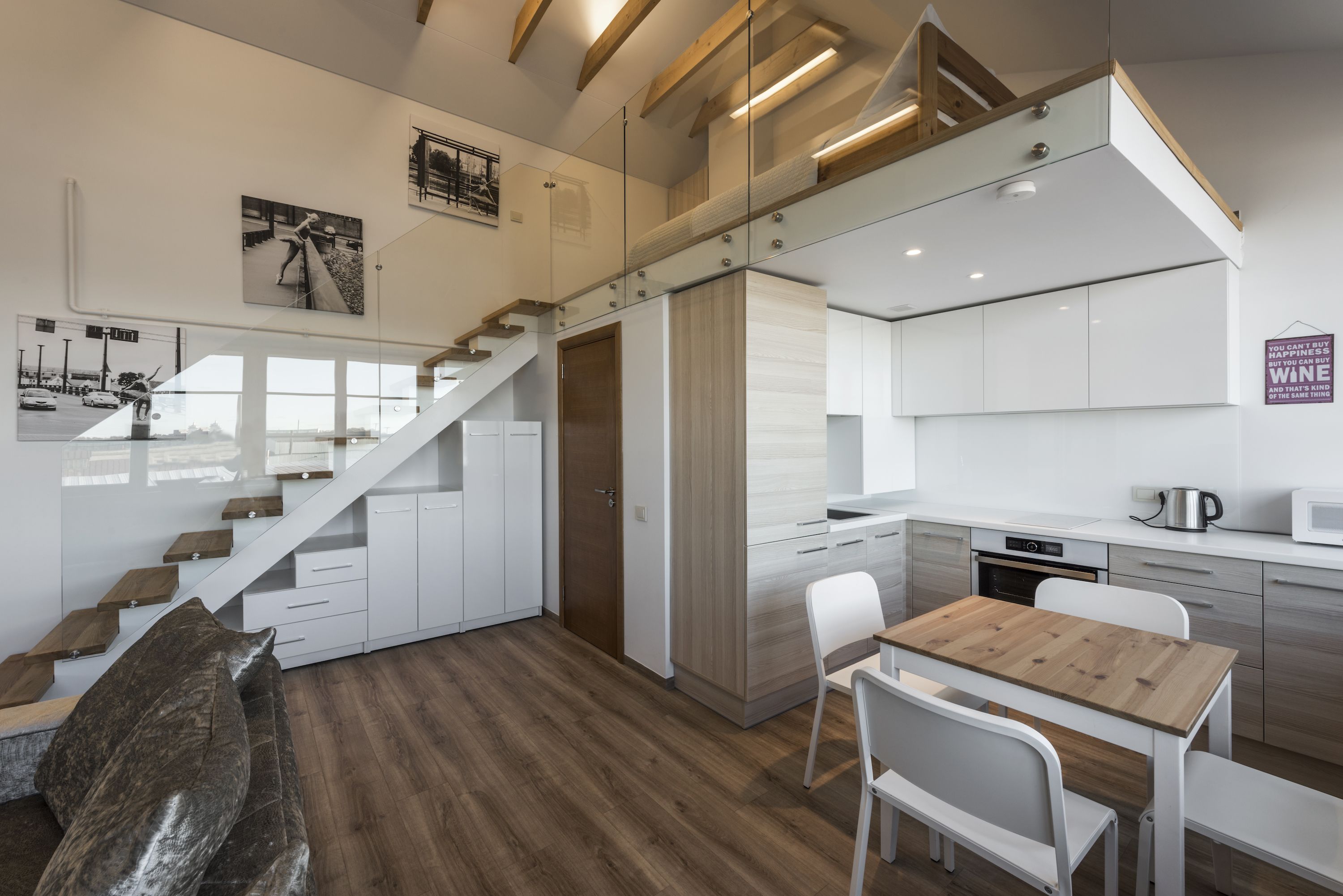 Eine moderne Küche mit weißen Schränken, einem Holztisch und einer Treppe mit Glastrennwand.