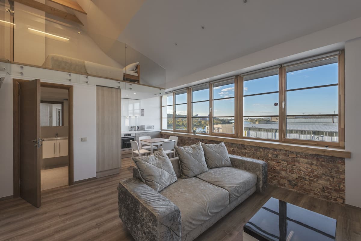 A modern living room with a large window, a sofa, and a kitchen area.