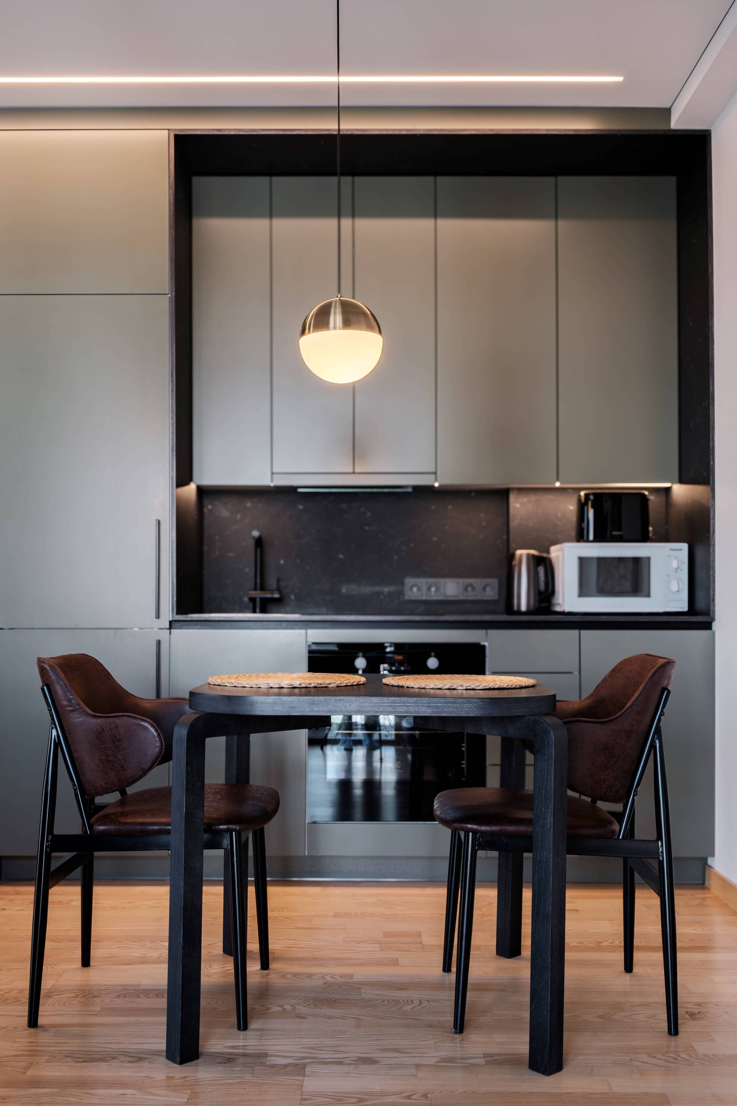 A modern kitchen with a dining table and chairs, a hanging light fixture, and built-in appliances.