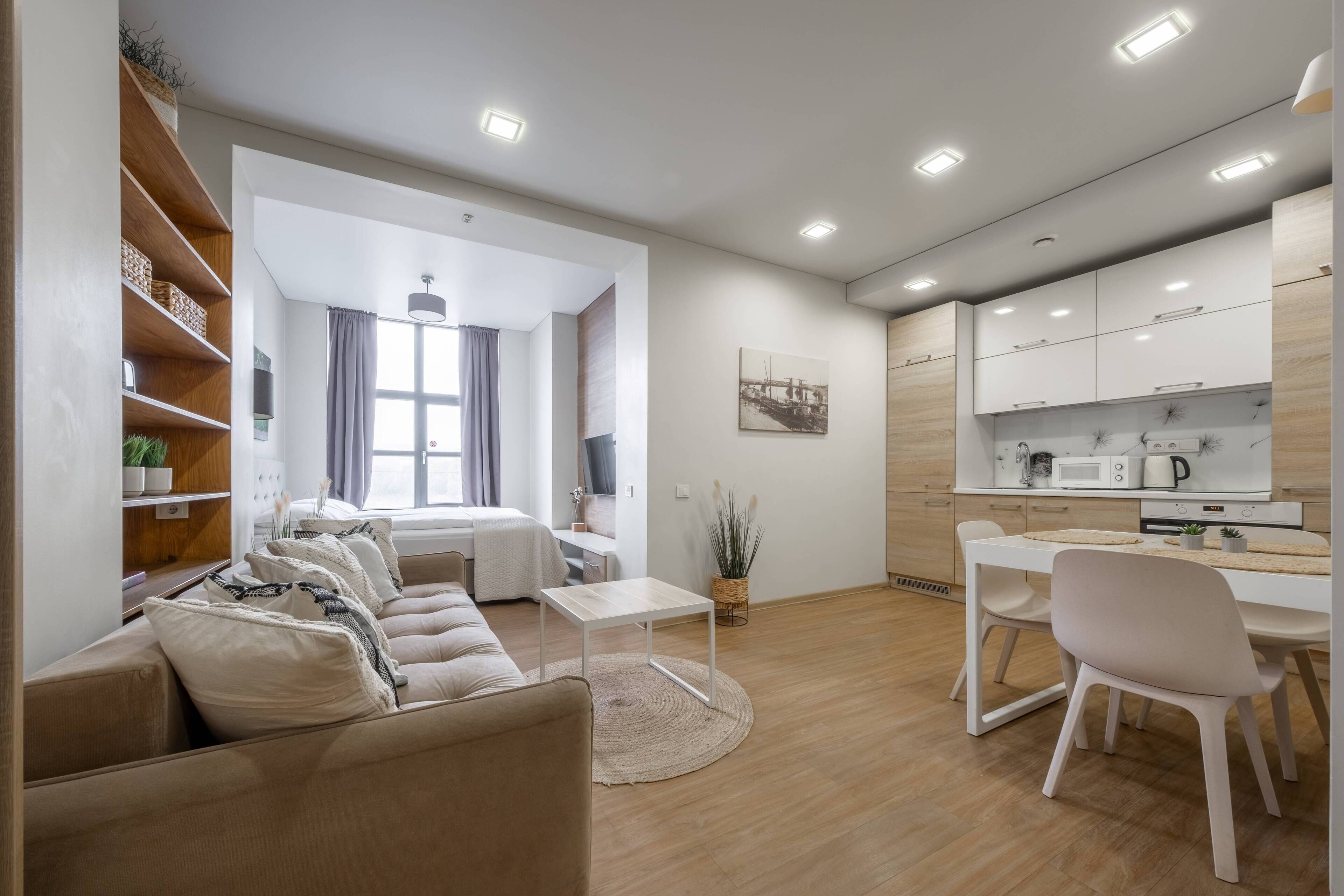 A modern living room with a sofa, a dining table, and a kitchen area with cabinets and appliances.