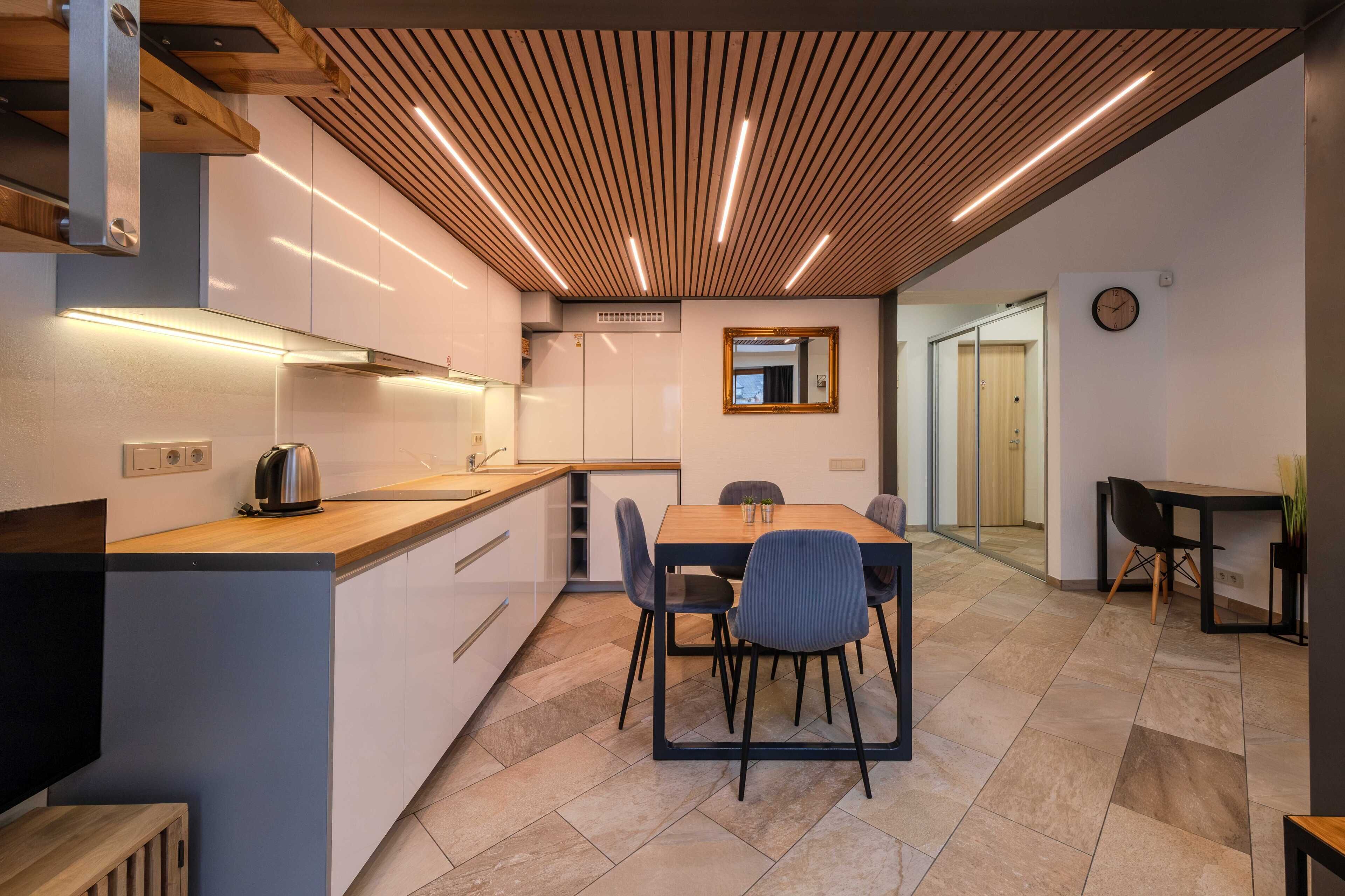 Una cocina moderna con techo de madera, una zona de comedor con mesa y sillas, y una mesita auxiliar con una planta.