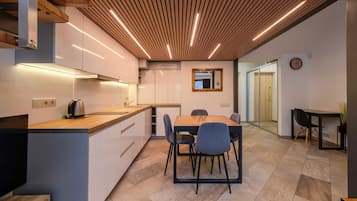 Una cocina moderna con techo de madera, una zona de comedor con mesa y sillas, y una mesita auxiliar con una planta.