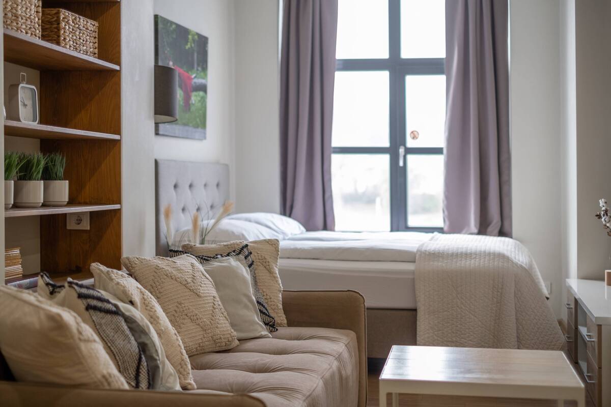 A bedroom with a bed, a sofa, a small table, and a shelf with decorative items.