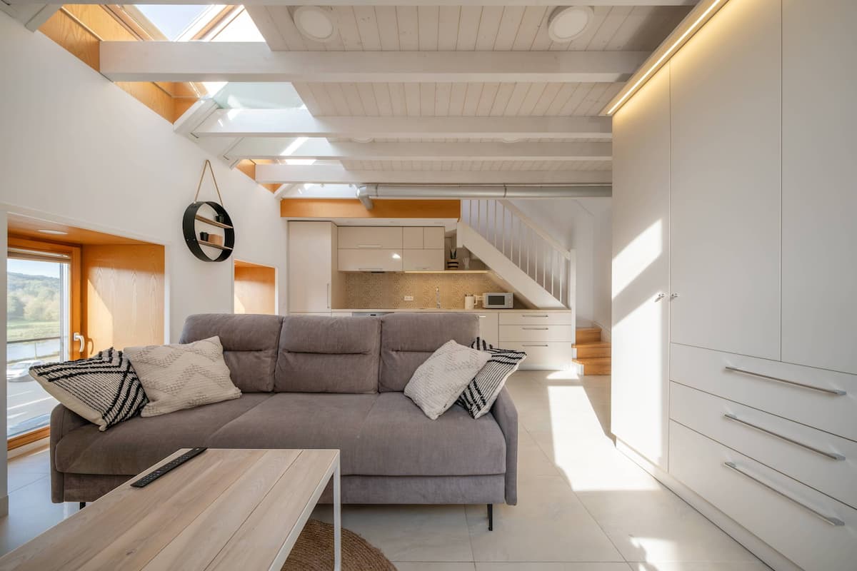 A modern living room with a grey sofa, wooden coffee table, and a kitchen in the background.