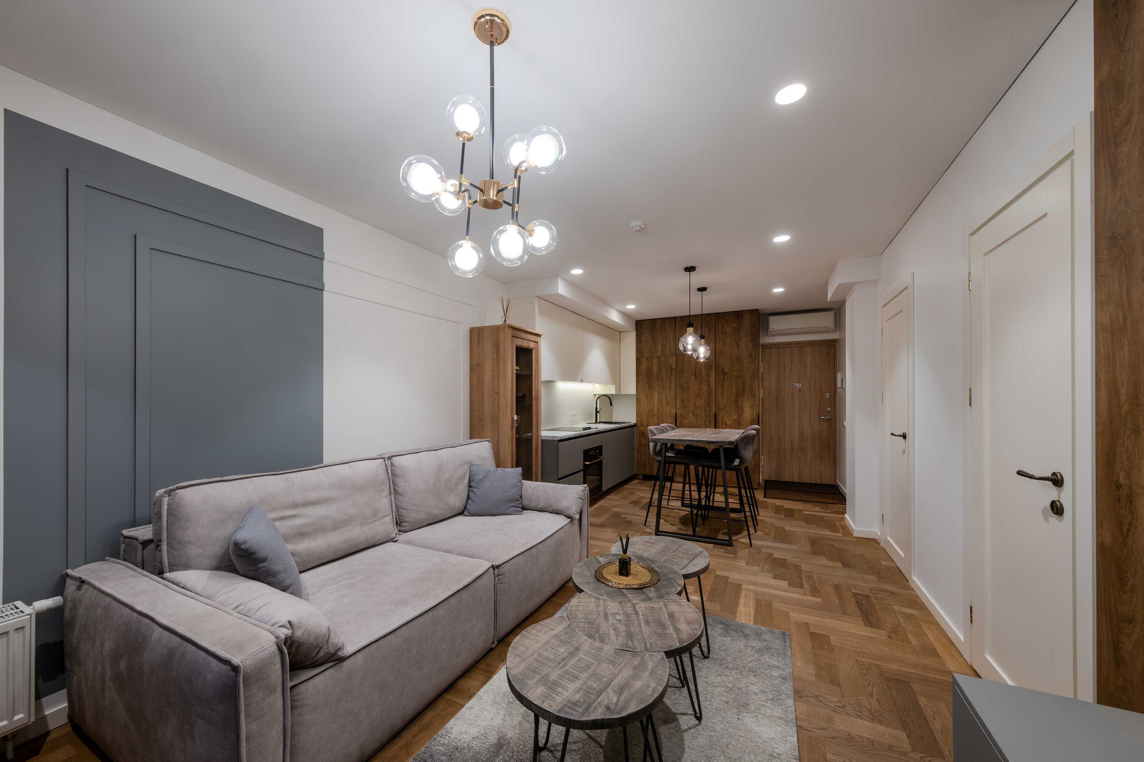 A modern living room with a grey sofa, a dining area with a table and chairs, and a kitchen in the background.