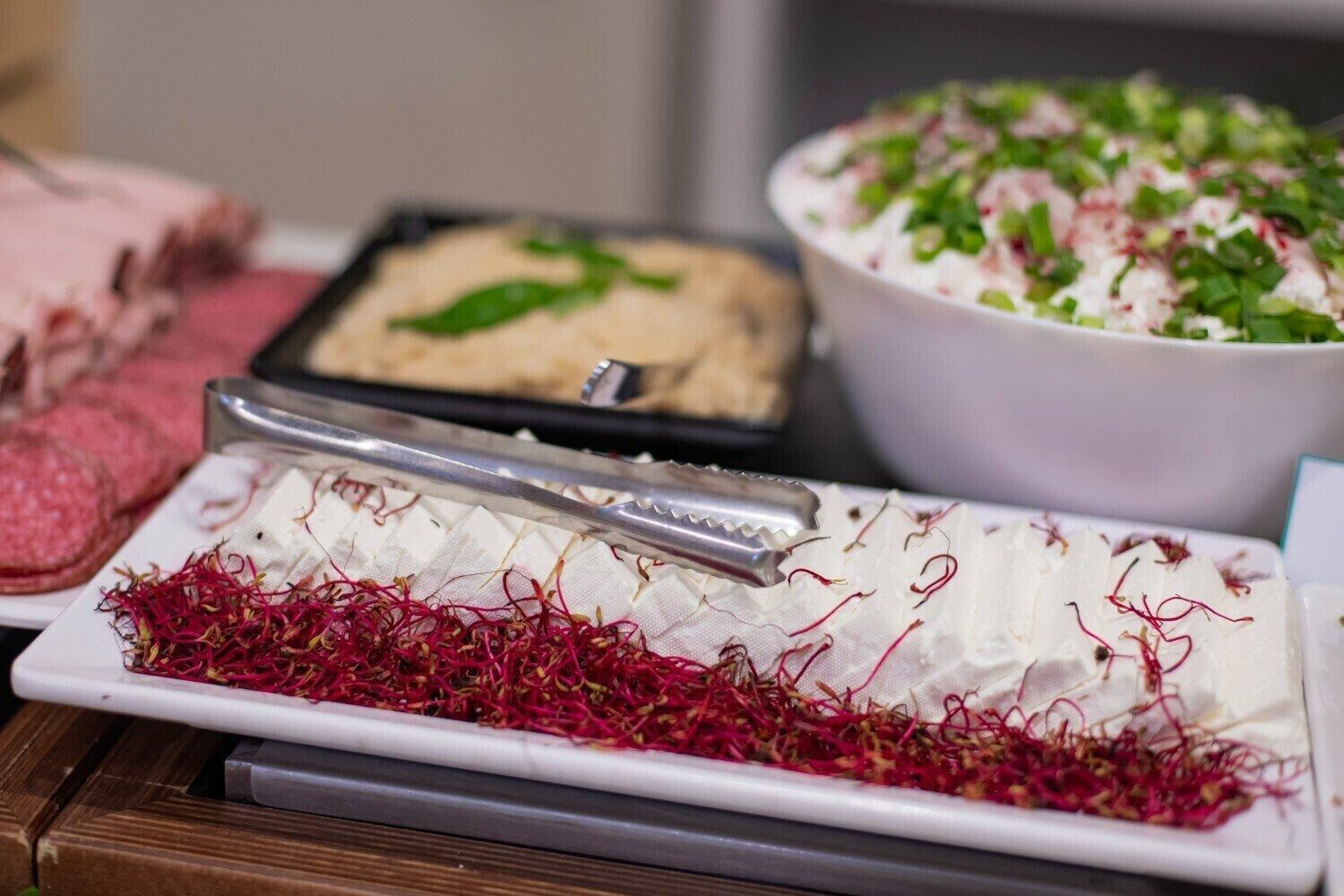 A variety of food items on a table, including a dish with shredded red vegetables, a bowl of salad with green toppings, and a tray of sliced meat.