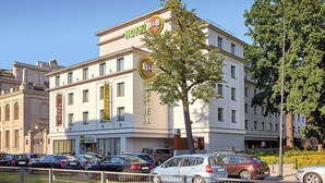 A hotel with multiple floors, a prominent B&B sign, and a parking lot with several cars. - B&B Hotel Łódź Centrum (Lodz)