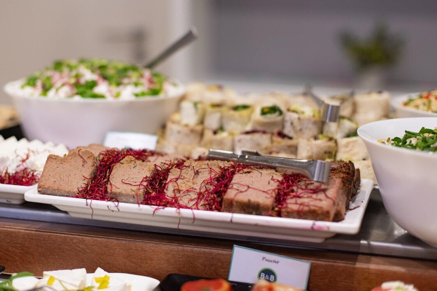 Un buffet proposant divers plats, dont un plat principal agrémenté d’une garniture rouge, et une pancarte indiquant « Pâtisseries ».