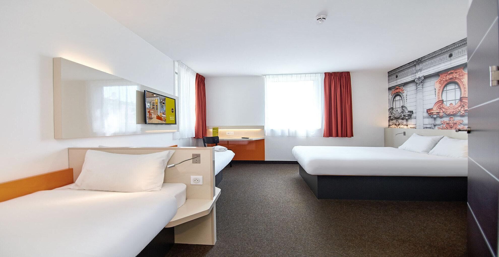 Une chambre d’hôtel avec deux lits, un bureau, une chaise, un grand miroir et un tableau au mur.