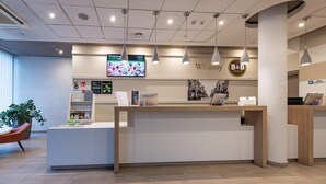 A reception desk with a digital screen displaying information, a sign for Witamy Hotels, and a modern interior design with a brick wall and wooden flooring. - B&B Hotel Łódź Centrum (Lodz)