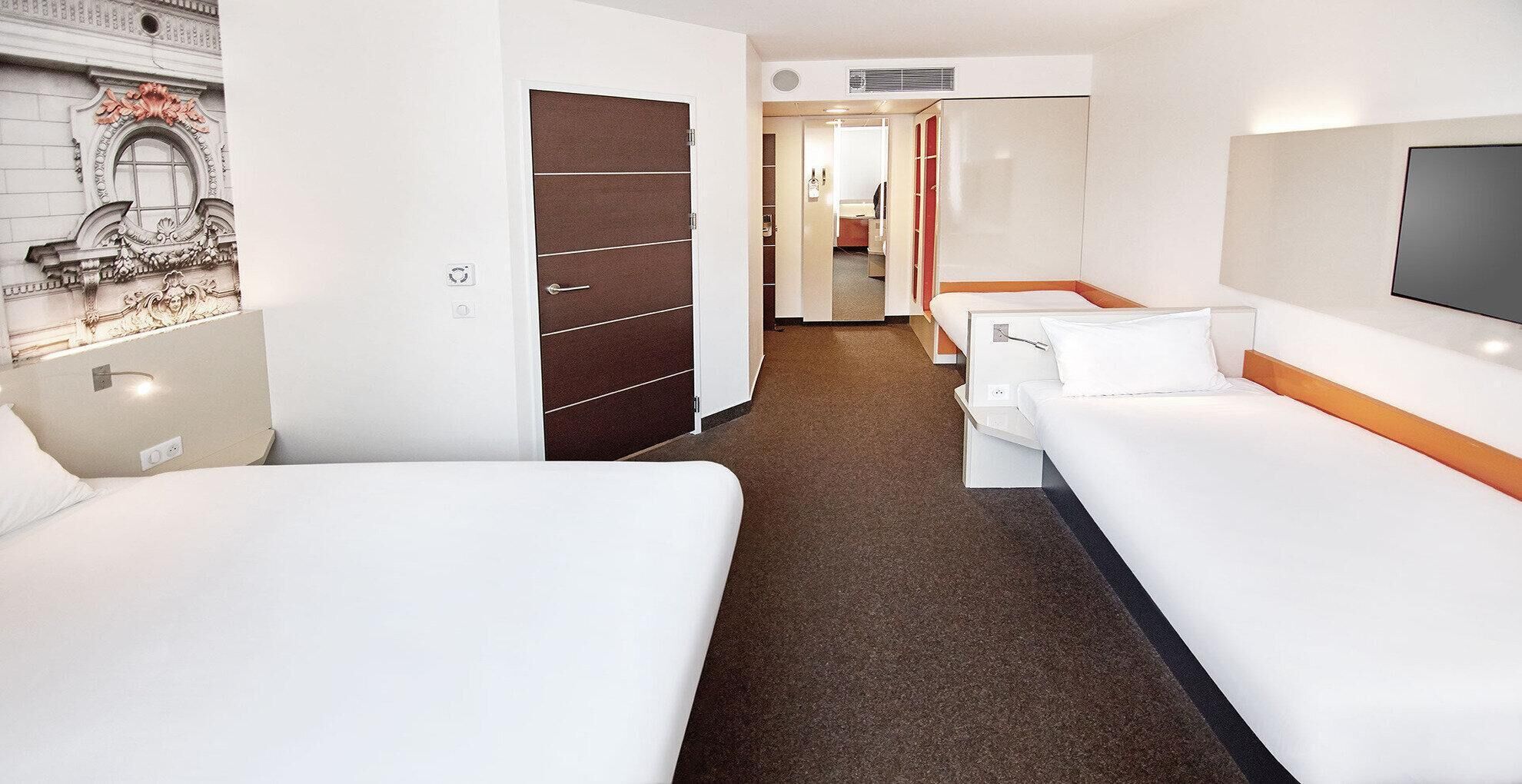A hotel room with two beds, a wardrobe, a TV, and a bathroom visible through an open door.